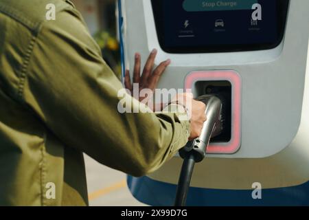 Image rognée du propriétaire ev prenant la prise de la station de charge publique Banque D'Images