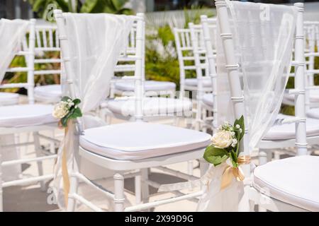 Gros plan d'une disposition élégante des sièges pour un mariage ou une cérémonie romantique avec chaises et coussins blancs, drapés dans un tissu transparent Banque D'Images