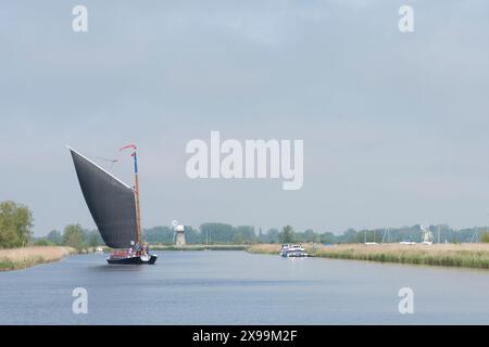 Les gens naviguent sur un bateau à voile traditionnel sur la rivière Bure, montrant St Benet's drainage Mill, et Thurne Dyke drainage Mill Banque D'Images