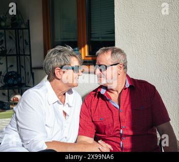 Femme souriante et homme dans des lunettes de soleil se regardant avec tendresse sur leur porche Banque D'Images