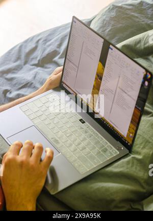 L'homme est assis dans son lit derrière son ordinateur portable. Photo de haute qualité Banque D'Images