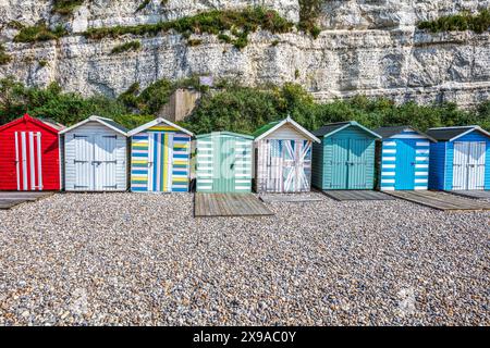 Rangée de cabanes de plage sur Beer Beach, Devon, Royaume-Uni Une rangée de cabanes de plage colorées se dresse devant une falaise de craie, chacune peinte dans des motifs différents et lumineux Banque D'Images