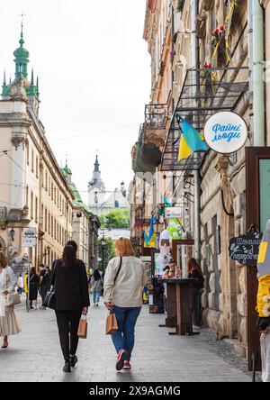 LVIV, UKRAINE - mai. 19, 2024 : deux jeunes femmes avec des sacs à provisions en papier sont vues se promener tranquillement dans la partie centrale de Lviv Banque D'Images