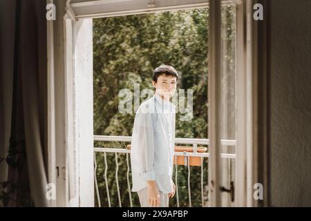 Vue latérale d'un adolescent souriant debout dans le balcon vu à travers l'entrée de la porte Banque D'Images