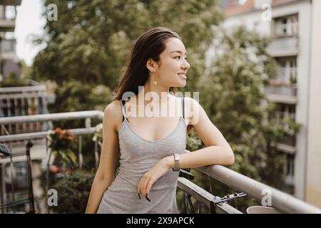 Femme souriante regardant loin tout en s'inclinant sur les balustrades du balcon Banque D'Images