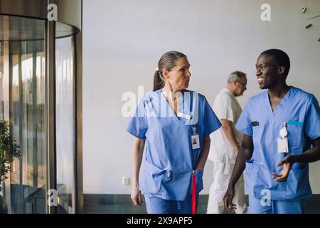 Les professionnels de santé multiraciaux en broussailles bleues discutent en marchant à l'hôpital Banque D'Images