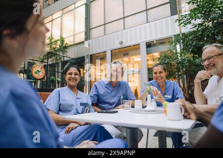 Heureux médecins hommes et femmes assis à table dans la cafétéria de l'hôpital Banque D'Images