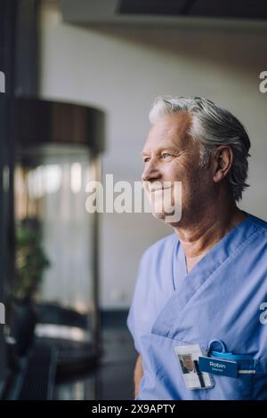 Médecin senior contemplatif souriant en gommage bleu à l'hôpital Banque D'Images