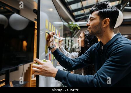 Entrepreneurs masculins et féminins écrivant sur des notes adhésives lors d'une réunion d'affaires au bureau Banque D'Images