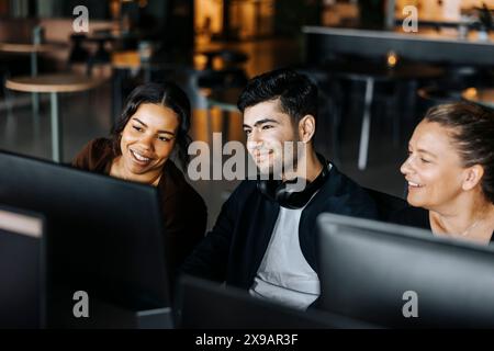 Souriant hommes et femmes entrepreneurs partageant l'écran d'ordinateur tout en étant assis au bureau Banque D'Images