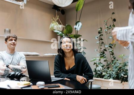 Souriant jeune femme freelance assis avec un ordinateur portable en réunion au bureau Banque D'Images