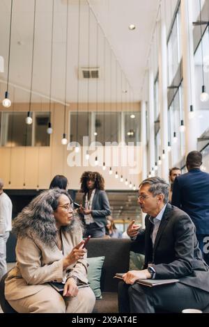 Entrepreneur masculin senior discutant des stratégies commerciales avec une déléguée féminine assise sur le canapé au centre de congrès Banque D'Images