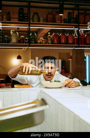 Chef masculin concentré versant de l'huile de vinaigrette dans un saladier à la cuisine commerciale Banque D'Images