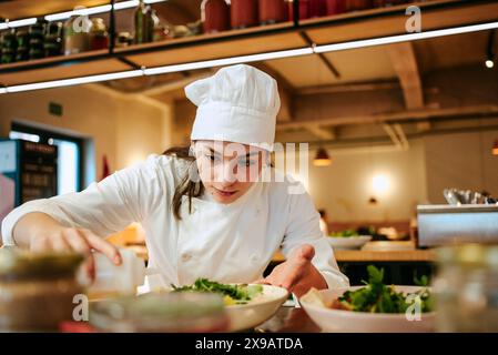 Gros plan d'une femme chef versant de l'huile de vinaigrette sur une salade à la cuisine commerciale Banque D'Images