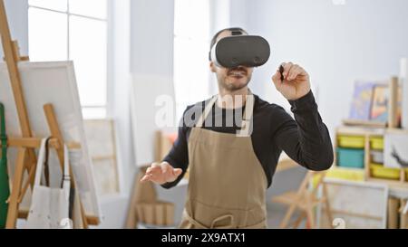 Homme portant un casque de réalité virtuelle faisant des gestes dans un studio d'art avec des chevalets et des peintures Banque D'Images