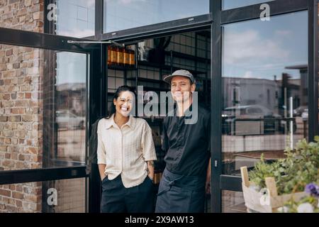 Propriétaire féminin heureux debout avec un collègue masculin à la porte du café Banque D'Images