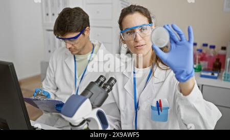 Dans un laboratoire bien équipé, une femme et un homme en blouse de laboratoire analysent des échantillons entourés d’équipements scientifiques. Banque D'Images