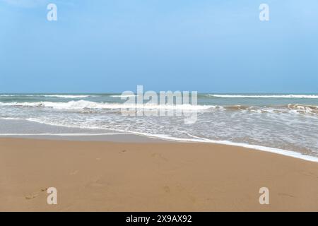 De douces vagues embrassent le rivage sablonneux sous un ciel bleu clair, invitant à la sérénité et à la détente. Banque D'Images