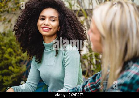 Deux femmes ayant une conversation décontractée à l'extérieur, l'une avec les cheveux bouclés et l'autre blonde, interaction amicale, cadre naturel, mode décontractée, fema Banque D'Images