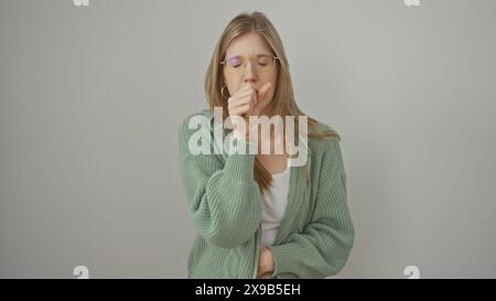 Une femme blonde en vêtements décontractés toussant dans sa main sur un fond blanc Banque D'Images