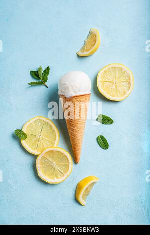 Boule de crème glacée au citron dans un cône de gaufrette et tranches de citron sur fond bleu clair, vue de dessus. Composition créative tendance. Banque D'Images