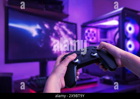 Configuration de jeu immersive avec un joueur jouant sur un PC de jeu avec manette de jeu, dans une salle de jeu avec un bureau de jeu et des lumières LED Banque D'Images