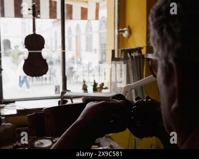 Silhouetté contre une fenêtre, un luthier travaille sur un instrument à cordes dans un atelier, avec des outils étalés sur le banc Banque D'Images