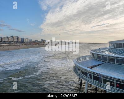 Large vue sur la mer et la plage depuis une jetée, avec des bâtiments au loin et un ciel partiellement nuageux, la plage de scheveningen avec jetée et le Banque D'Images