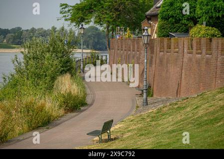 Chemin sinueux le long d'un mur de briques avec des bancs de parc et des lampes, bordé d'arbres verts et de maisons, la promenade de Rees sur le Rhin avec des arbres verts dans Banque D'Images