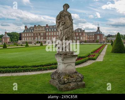 Impressionnante figure en pierre devant un grand château, entouré d'un jardin bien entretenu et de fleurs colorées, vieux château en briques rouges avec des tours et un Banque D'Images