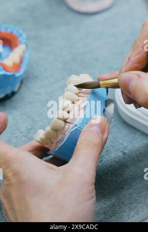 Vue rapprochée des mains d'un technicien dentaire tenant une brosse à dents, se concentrant sur la fabrication de prothèses à l'aide de matériaux dentaires et d'outils pour les soins buccaux. Banque D'Images