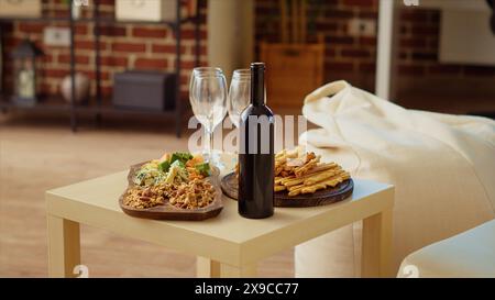 Plan panoramique du tableau des hors-d'œuvre et plateau de fromage gastronomique mis en place par les hôtes pour accueillir correctement les invités arrivant bientôt à la réunion sociale. Bouteille de vin et verres à côté de la nourriture dans la maison confortable, gros plan Banque D'Images