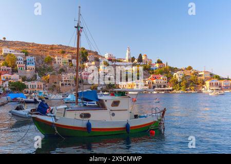 Vue panoramique des maisons colorées et des bateaux dans le port de l'île de Symi, Grèce, au coucher du soleil Banque D'Images