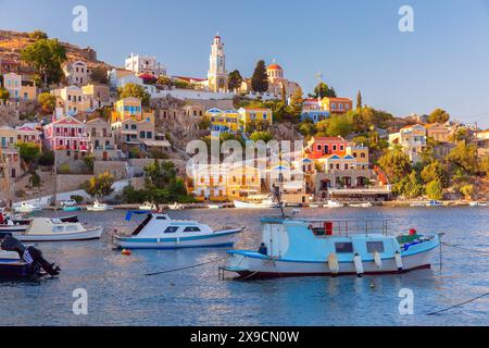 Vue panoramique des maisons colorées et des bateaux dans le port de l'île de Symi, Grèce, au coucher du soleil Banque D'Images