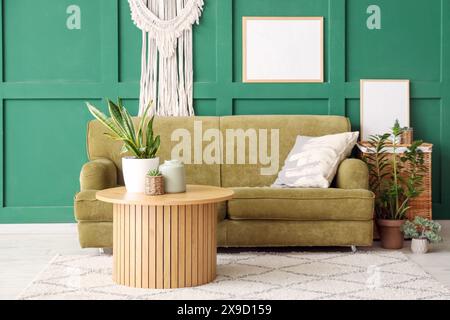 Canapé confortable avec coussin, table basse avec plantes et cadres sur le mur dans le salon Banque D'Images