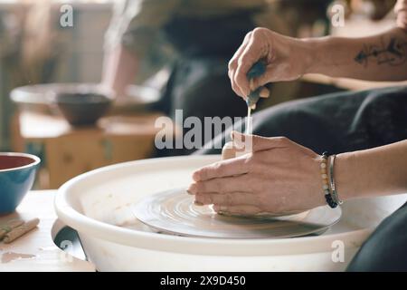 Main d'artisan féminin méconnaissable pressant l'eau hors de l'éponge tout en travaillant avec de l'argile sur la roue de potier, gros plan Banque D'Images