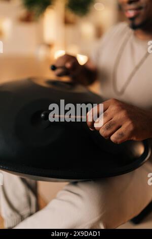 Plan vertical recadré d'un homme africain calme méconnaissable jouant de la musique ethnique traditionnelle sur du glucophone à l'aide de bâtons assis sur le sol dans la posture du lotus. Banque D'Images