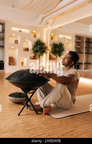 Plan vertical d'un homme africain heureux jouant de la musique ethnique traditionnelle en utilisant du glucophone assis sur le sol dans la pose de lotus. Rythme de batterie masculin noir serein Banque D'Images