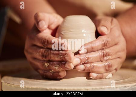 Vue avant gros plan de mains douces femmes façonnant l'argile sur la roue de poterie appréciant le processus d'artisanat à la lumière du soleil Banque D'Images