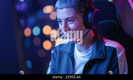 Excité joueur féminin jouant au jeu vidéo en ligne sur ordinateur. Gros plan Portrait de jeune femme élégante dans les écouteurs se battant dans le tournoi PvP avec d'autres joueurs, parler avec l'équipe sur microphone. Banque D'Images