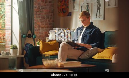 Portrait d'un bel homme assis sur le canapé, à l'aide d'un ordinateur portable dans élégant Loft Apartment le jour ensoleillé. Créatif masculin concentré, travaillant sur le projet en ligne, pensant aux résultats futurs. Banque D'Images