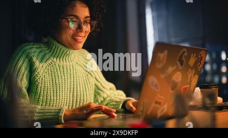 Positive Black Female Software Engineer Coding sur ordinateur portable, travaillant avec inspiration dans son studio. Femme étudiant tard dans la soirée. Freelancer moderne chez Remote Work concept. Banque D'Images