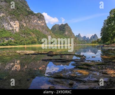 Paysage de montagnes karstiques sur la rivière Li avec réflexion et premier plan pierreux. Yangshuo, Guilin, Guangxi, Chine. Banque D'Images