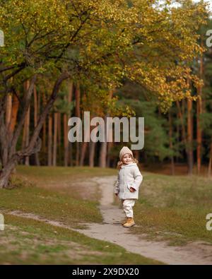 Une belle petite fille souriante marche à travers la forêt d'automne Banque D'Images