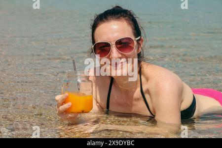 Femme souriante appréciant la boisson rafraîchissante dans la mer Banque D'Images