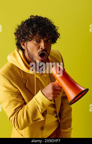 Homme en sweat à capuche jaune tient un mégaphone rouge et orange. Banque D'Images