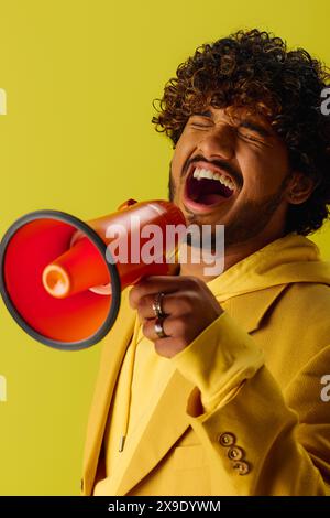 Beau jeune homme indien en costume jaune audacieux commande l'attention avec un mégaphone rouge et noir. Banque D'Images