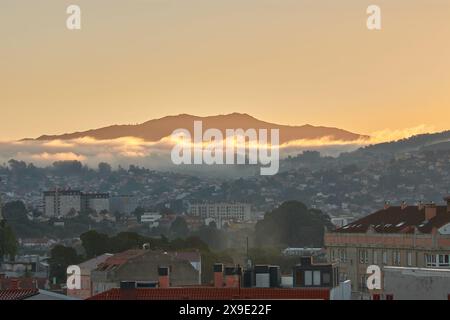 La lumière matinale baigne une ville de chaleur tandis que la brume roule sur la montagne en arrière-plan, créant un paysage serein Banque D'Images