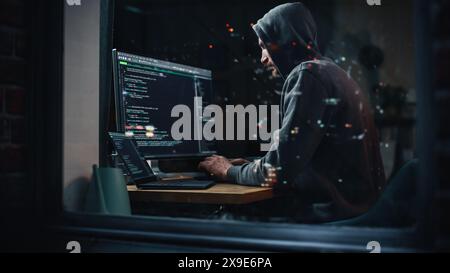Pirate utilisant un ordinateur de bureau pour perpétuer une cyberattaque, faire une attaque DDOS, envoyer des virus, des logiciels de phishing, des logiciels malveillants, vol de données privées, fraude par carte de crédit. Prise de vue dans la fenêtre de City Apartment. Banque D'Images