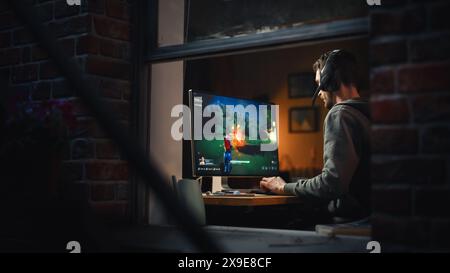 Jeux à la maison : Gamer streaming et jouer à des jeux vidéo en ligne sur ordinateur. Joueur masculin élégant profitant de 3D Shooter. Écran montrant Arcade Online Multiplayer PvP Battle. Concept de gameplay. Banque D'Images